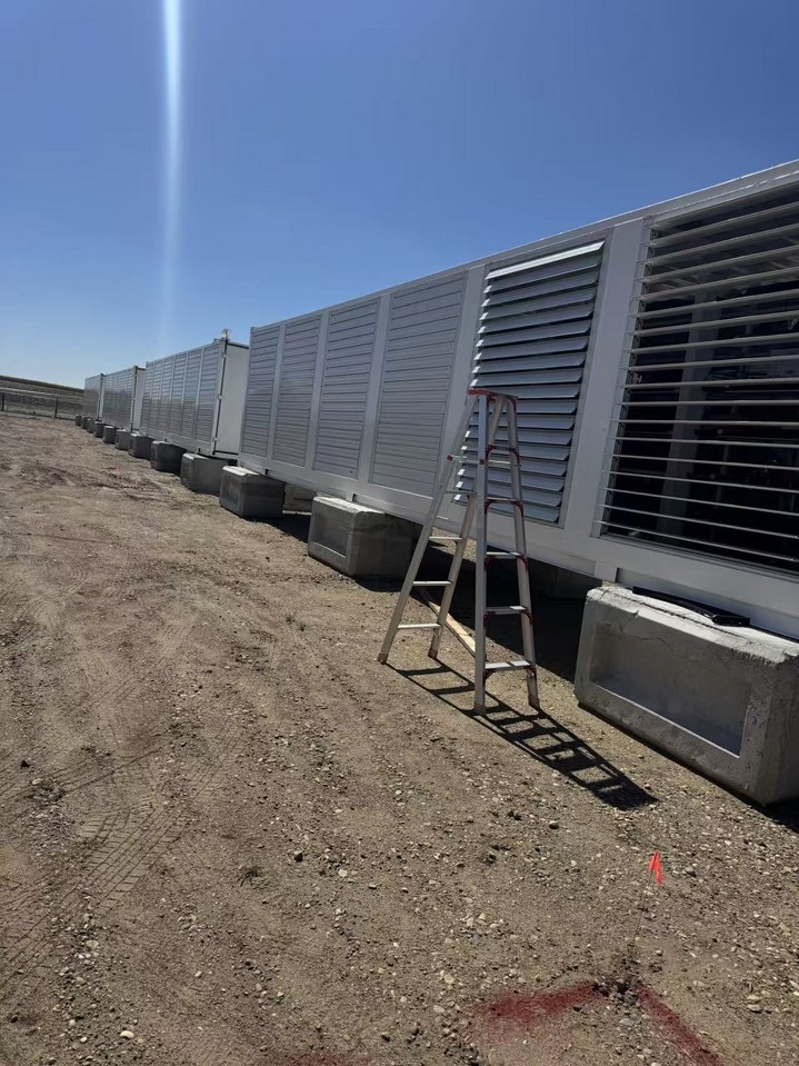 Long line of louvred containerized generator enclosures set on concrete blocks across a graded construction pad.